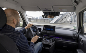 Aufnahme von der Rückbank über die Schulter des Fahrers im Hyundai Inster während der Fahrt über eine Brücke in Frankfurt